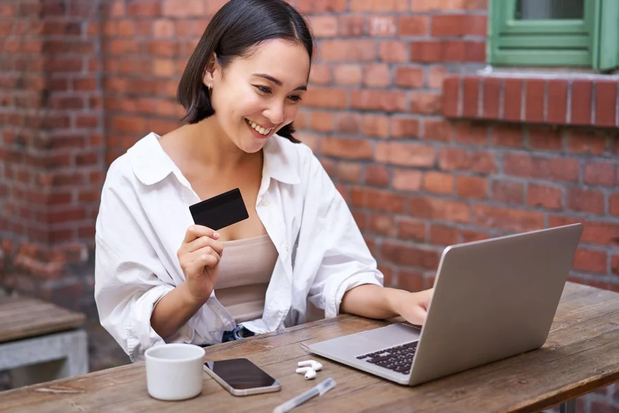 A smiling woman is taking out her credit card while online shopping through her laptop.